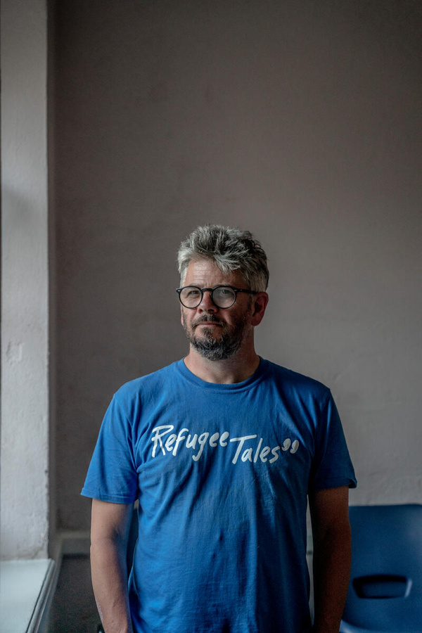 Man poses stood up against a wall.
