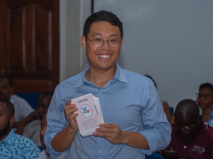 A smiling man holds up a card which reads 'Purpose' during a training session