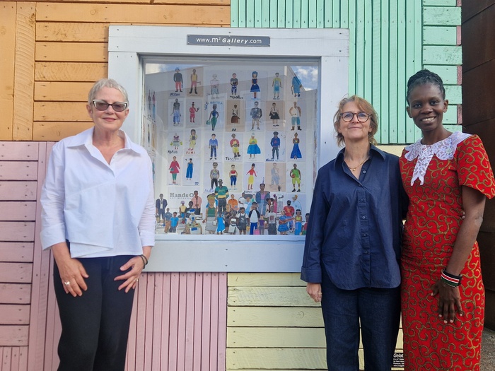 Three women stand in front of a window displaying paintings 