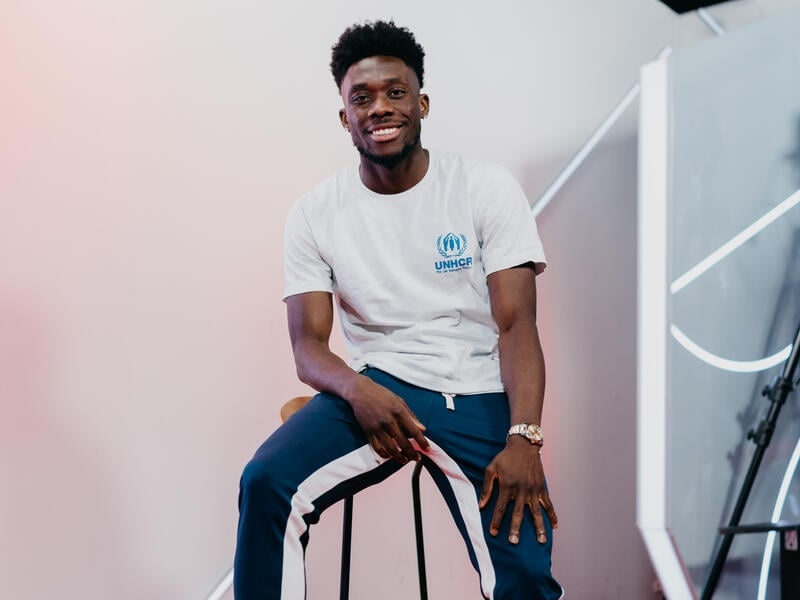 Alphonso Davies sits on a chair, a soccer ball under his foot.