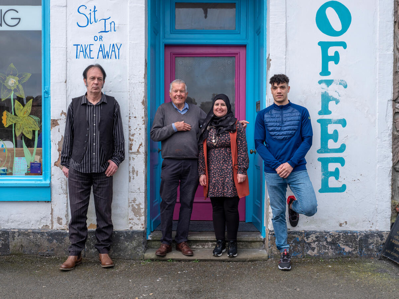 Woman and three men of varying ages pose for photo in the doorway of a café.