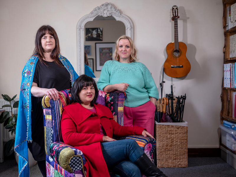 Three people pose in a music studio. 
