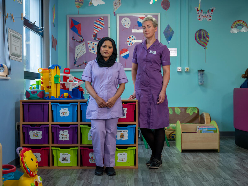 Two nurses pose for photo stood in hospital playroom.