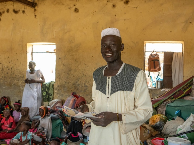 A young man holds some documents in a crowded room.