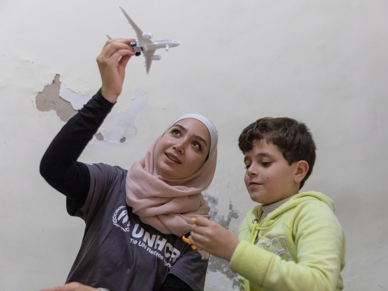 A young woman plays with a young boy with a plane toy.