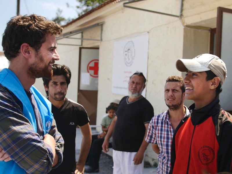 Theo James speaks with a teenage boy from Syria while other men gather around them.