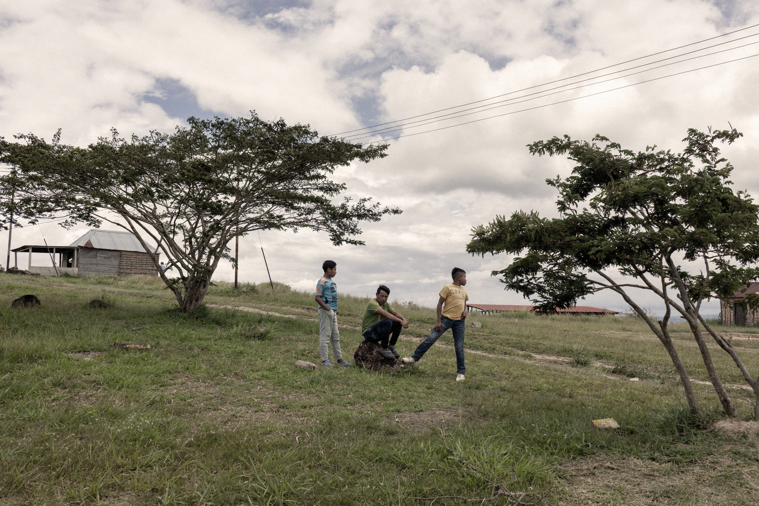 A young man sits on a rock as two friends stand either side