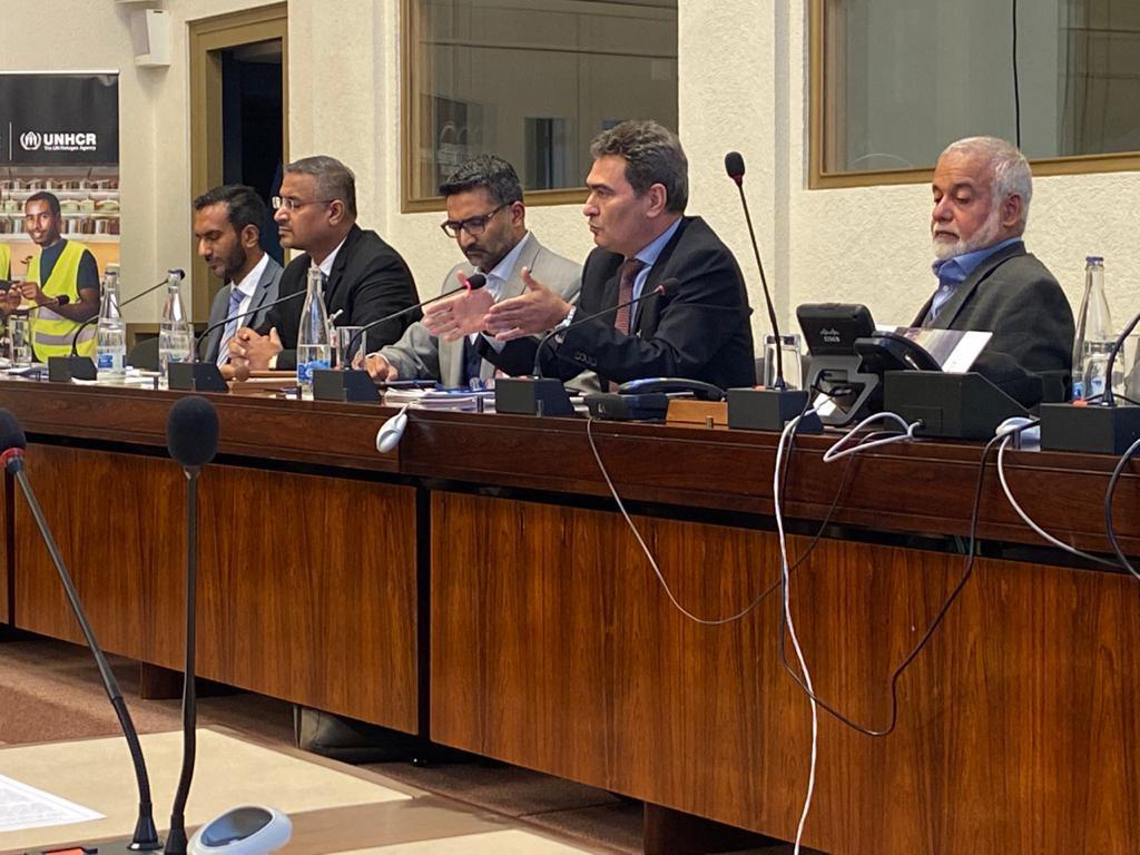 A group of five men, including Mr. Jamal, behind a podium with microphones and telephones.