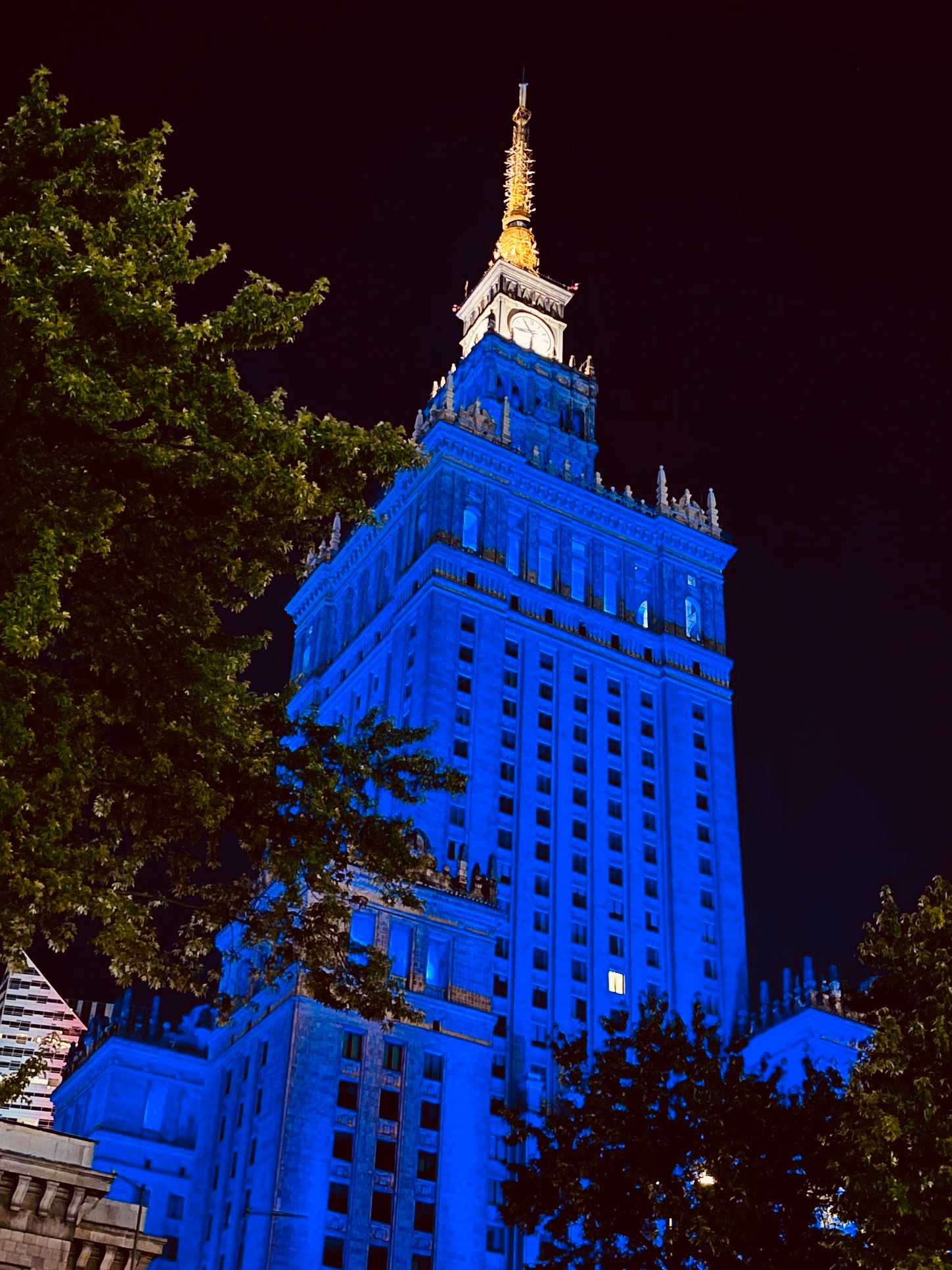 A high rise building lit up in blue with a white point