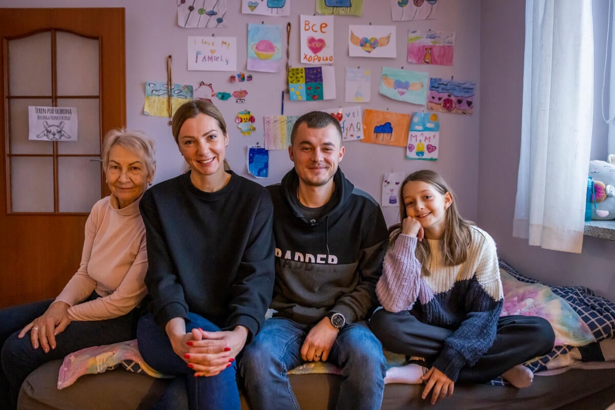 Dmytro and his family sit on the bed in his daughter's room at home.