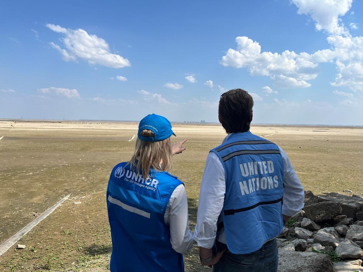Two UN staff members look out across flat land, one of them pointing into the distance