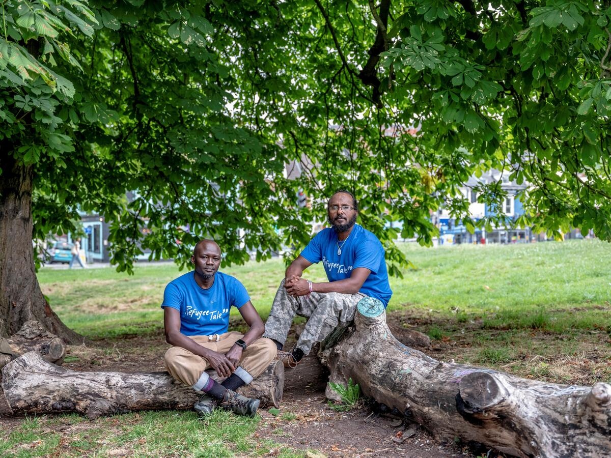 Two men pose seated in a park.