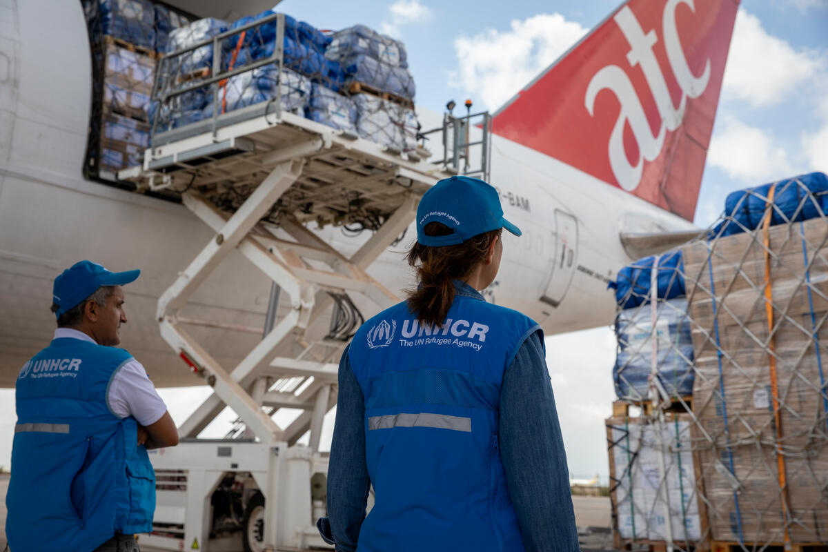 Two UNHCR staff members look on as emergency supplies are airlifted from an atc plane.