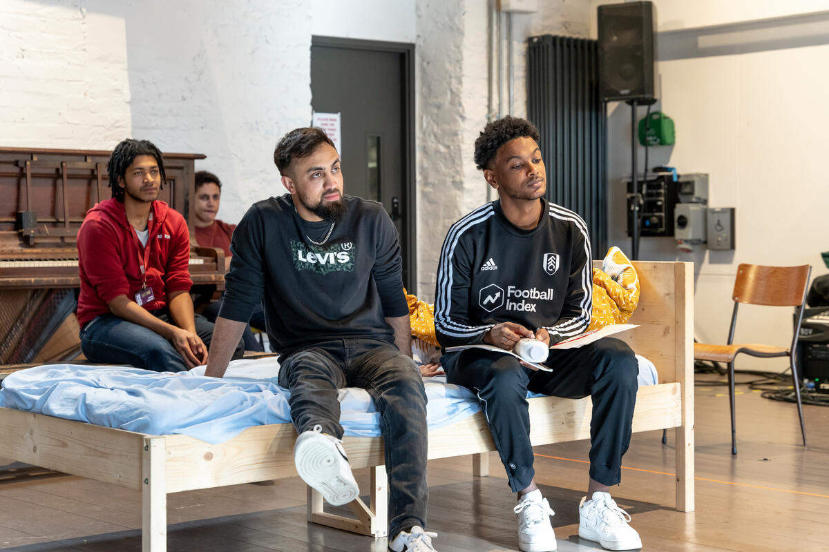 Two men sit on a bed.