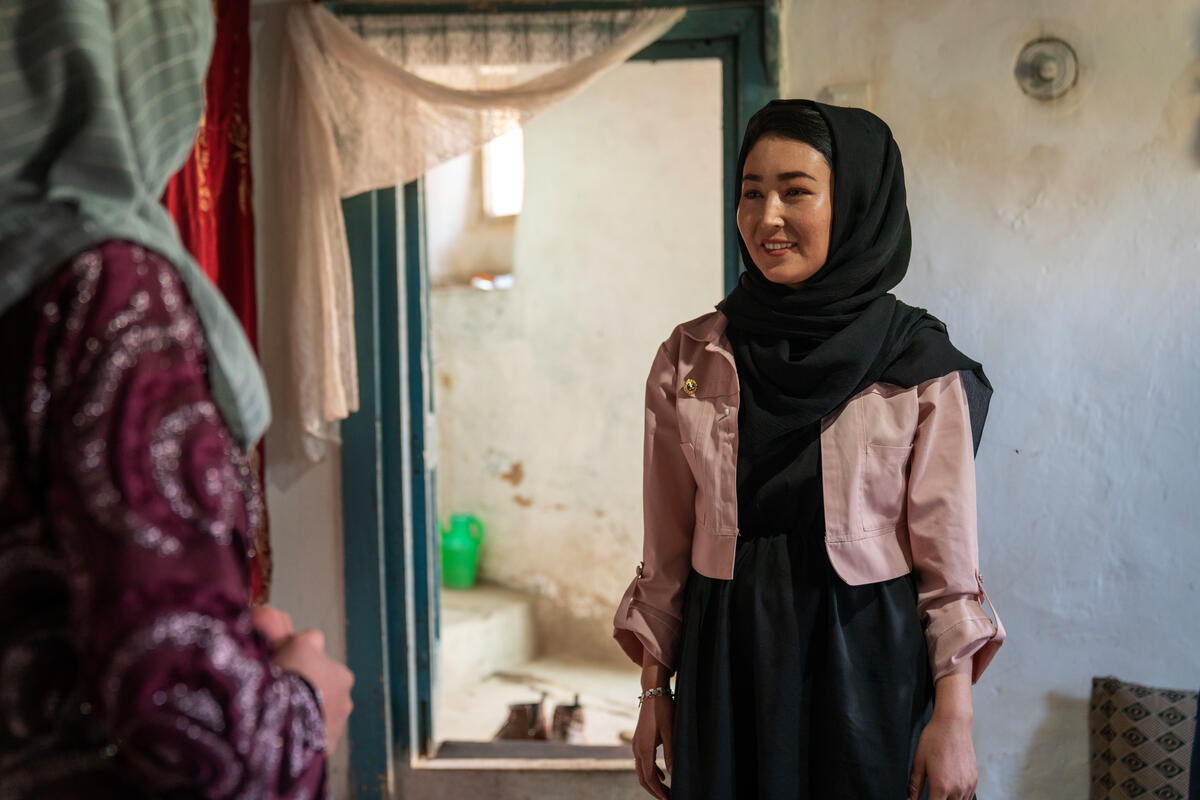 A young woman smiles as she talks to another woman in her home.