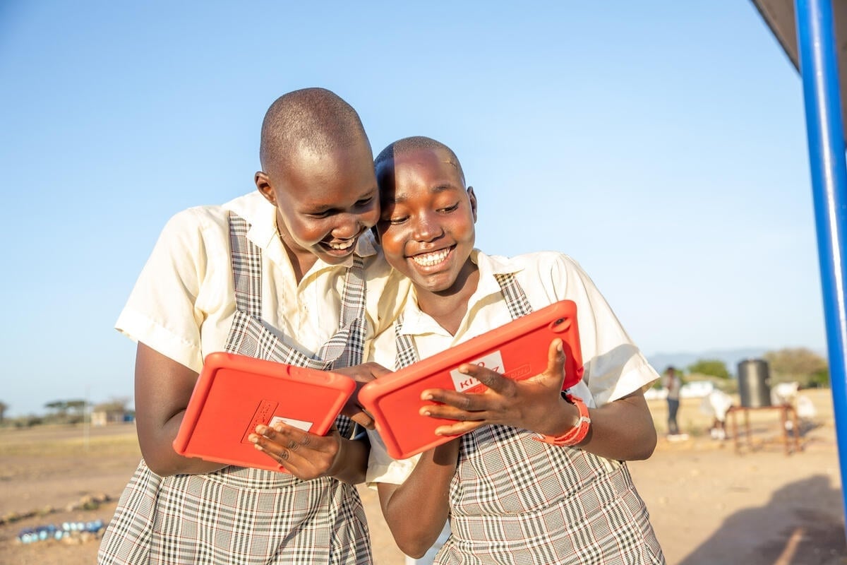 Two girls smiling as they use bright orange tablets.