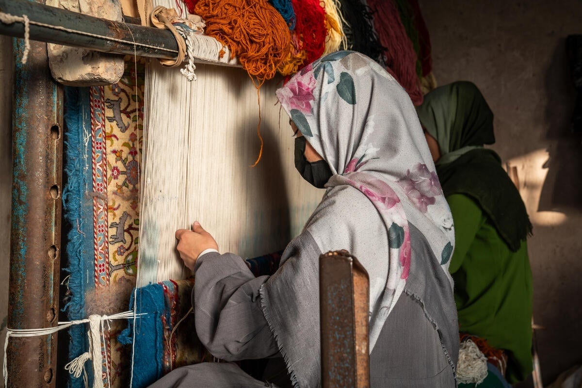 A woman weaving a carpet on a loom.