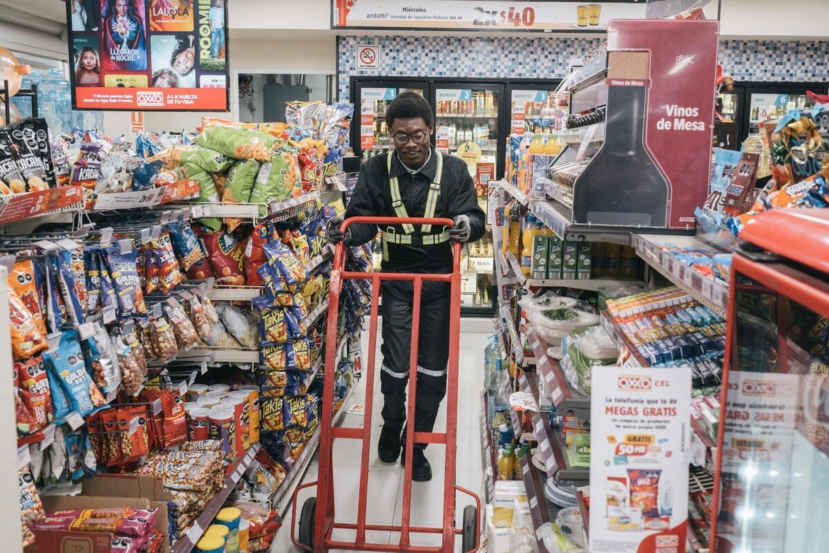 A man pushes a delivery trolley down the aisle of a convenience store.