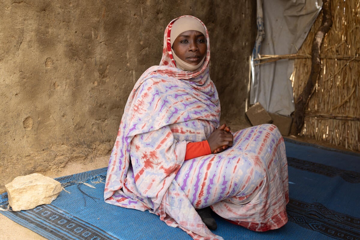 A woman sitting on a blue rug inside a shelter