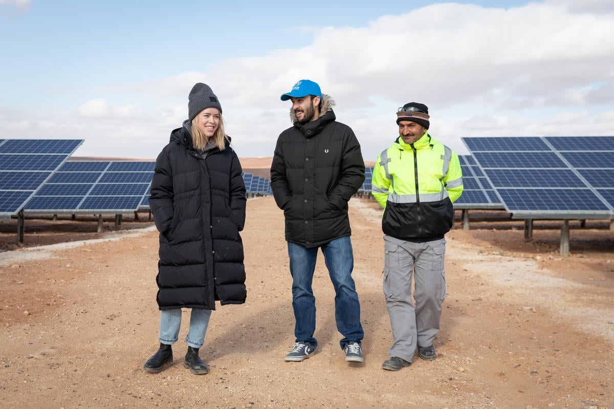 Tanya Burr walks through a solar panels field with two men.