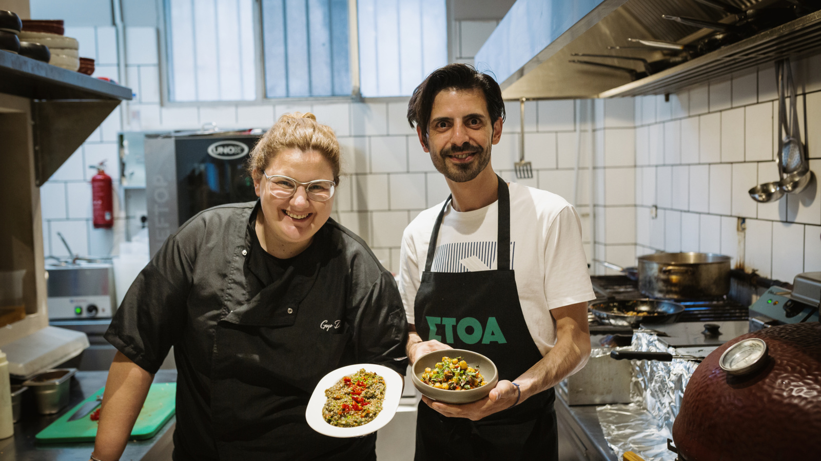 Two men hold two dishes in a professional kitchen.