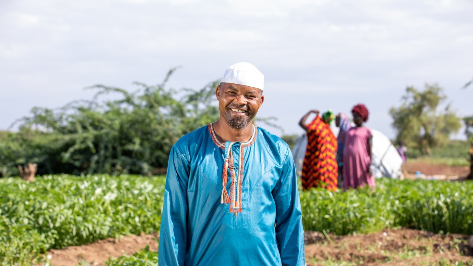 A smiling man stands in a field where crops grow.