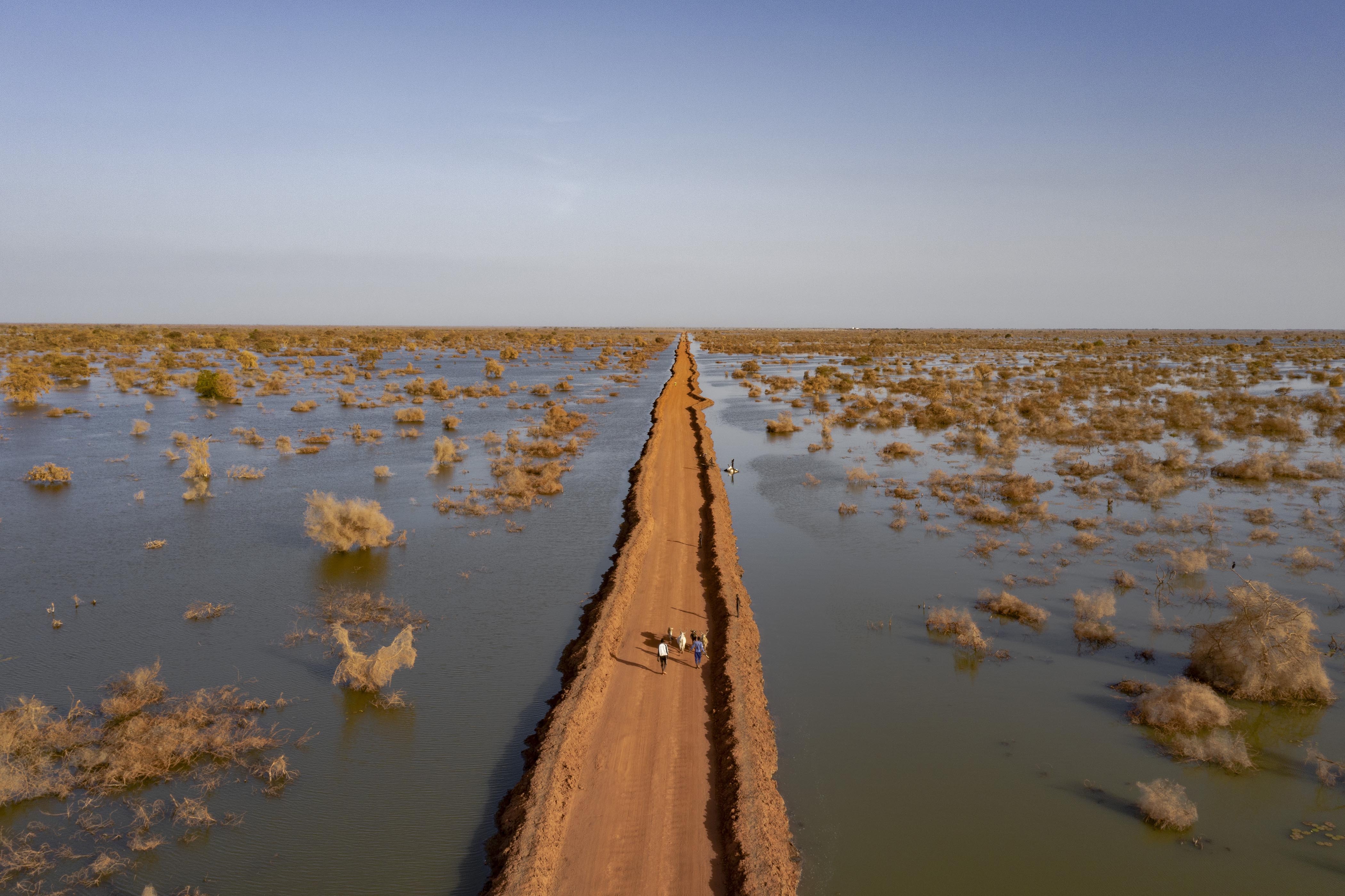 People walk along a diked road stretching to the horizon cutting through flood water
