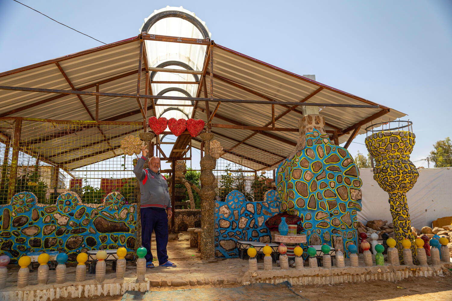 A man stands waving in front of an elaborately decorated plant nursery.