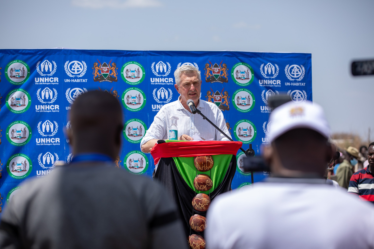 UNHCR's Filippo Grandi delivers a speech from a podium in a refugee camp.