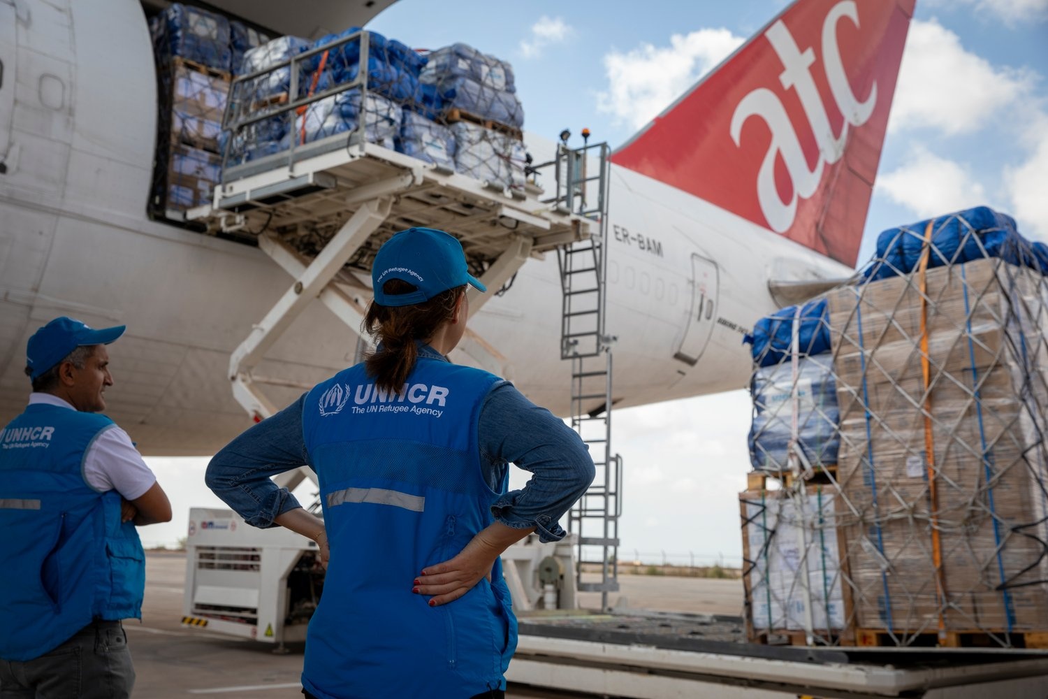 UN staff watch as aid supplies are unloaded from the back of an aircraft.