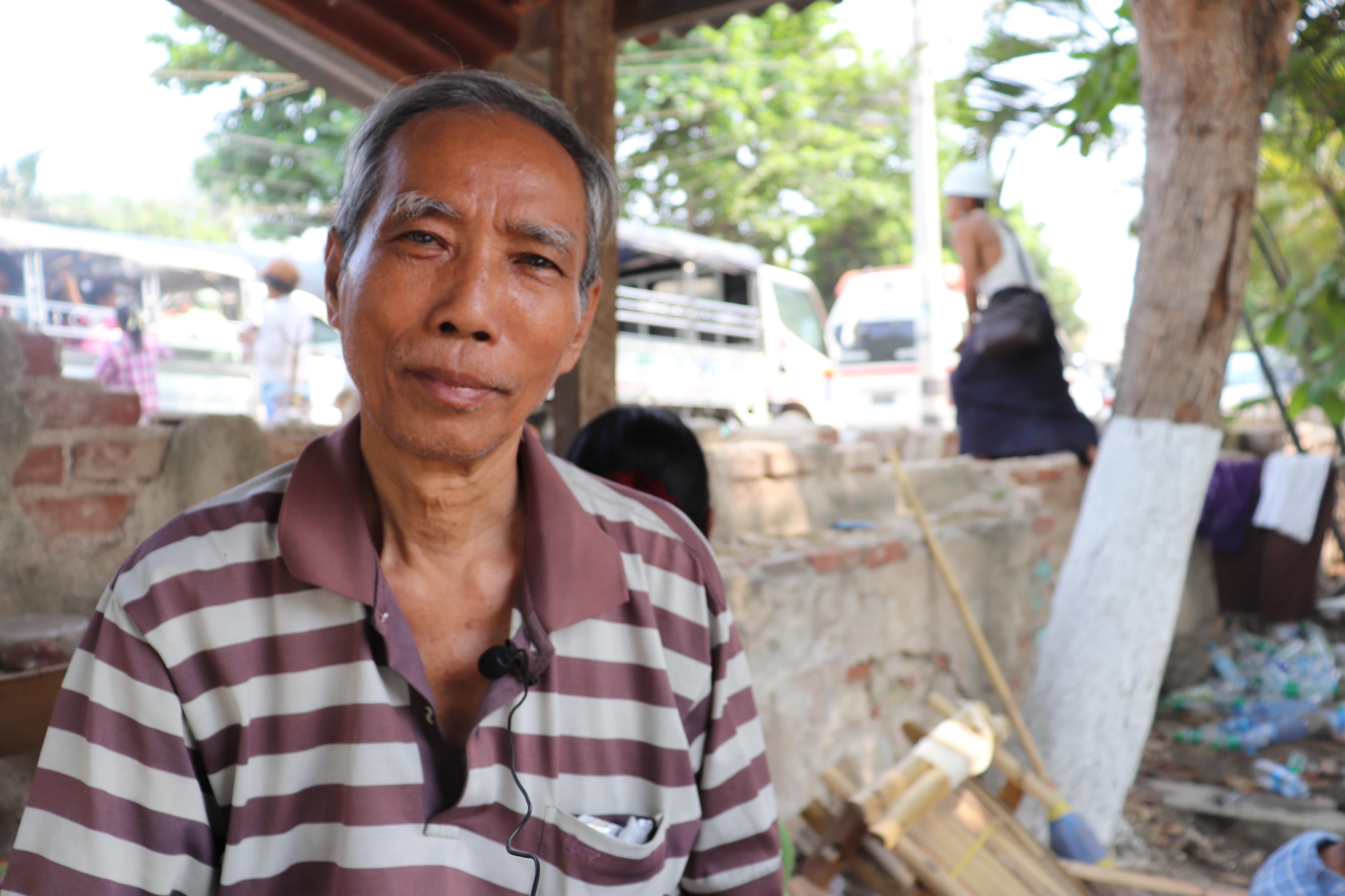 A man in a striped shirt sits outside in front of a brick wall