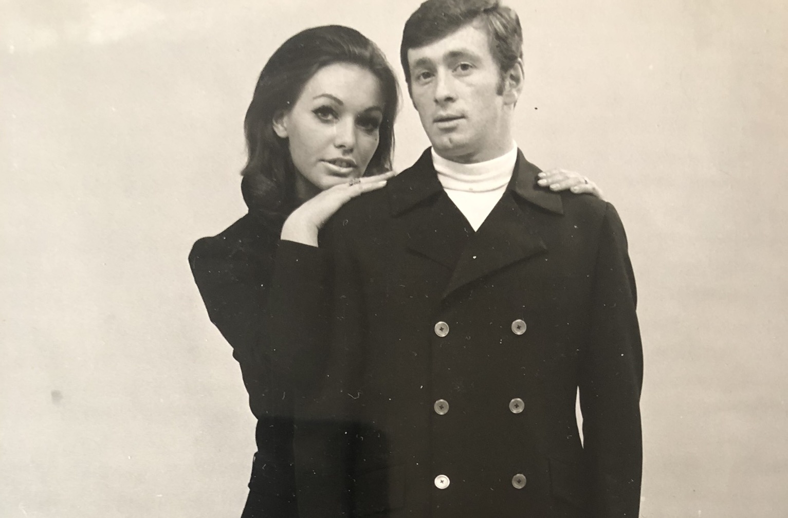 A man and a woman in 1960s clothing pose together in a sepia faded image
