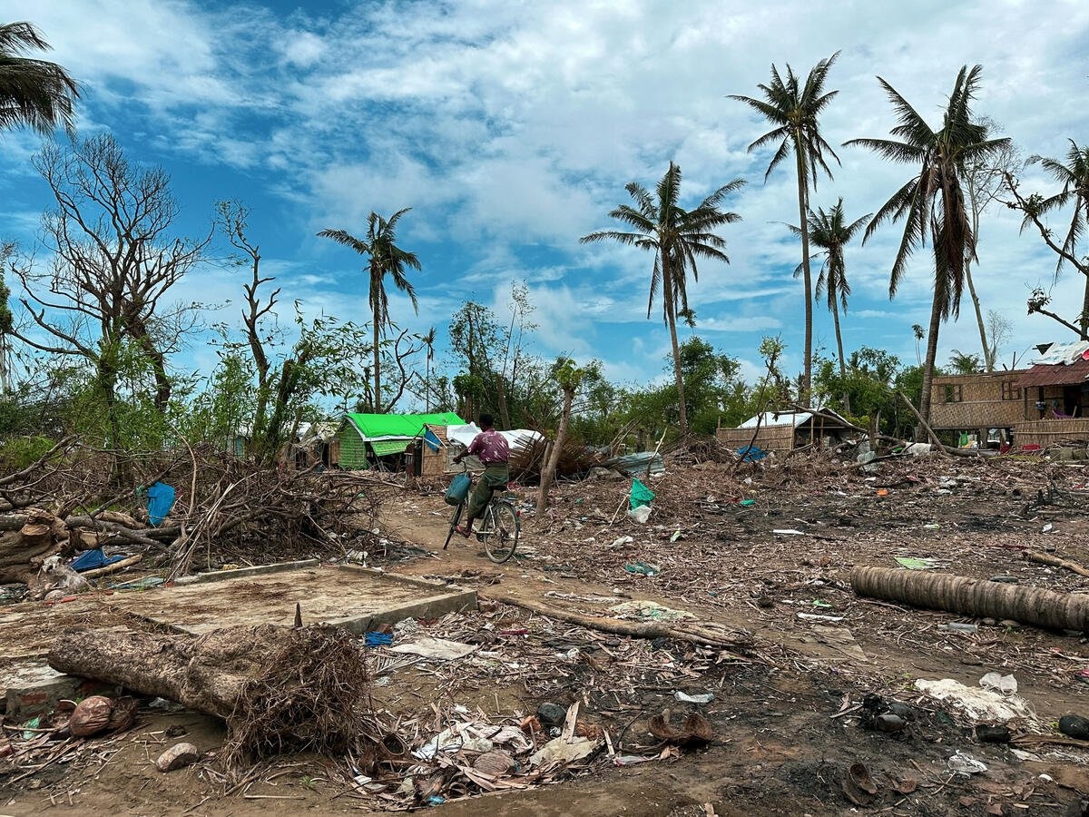 A person navigates a cyclone-damaged village on a bicycle.