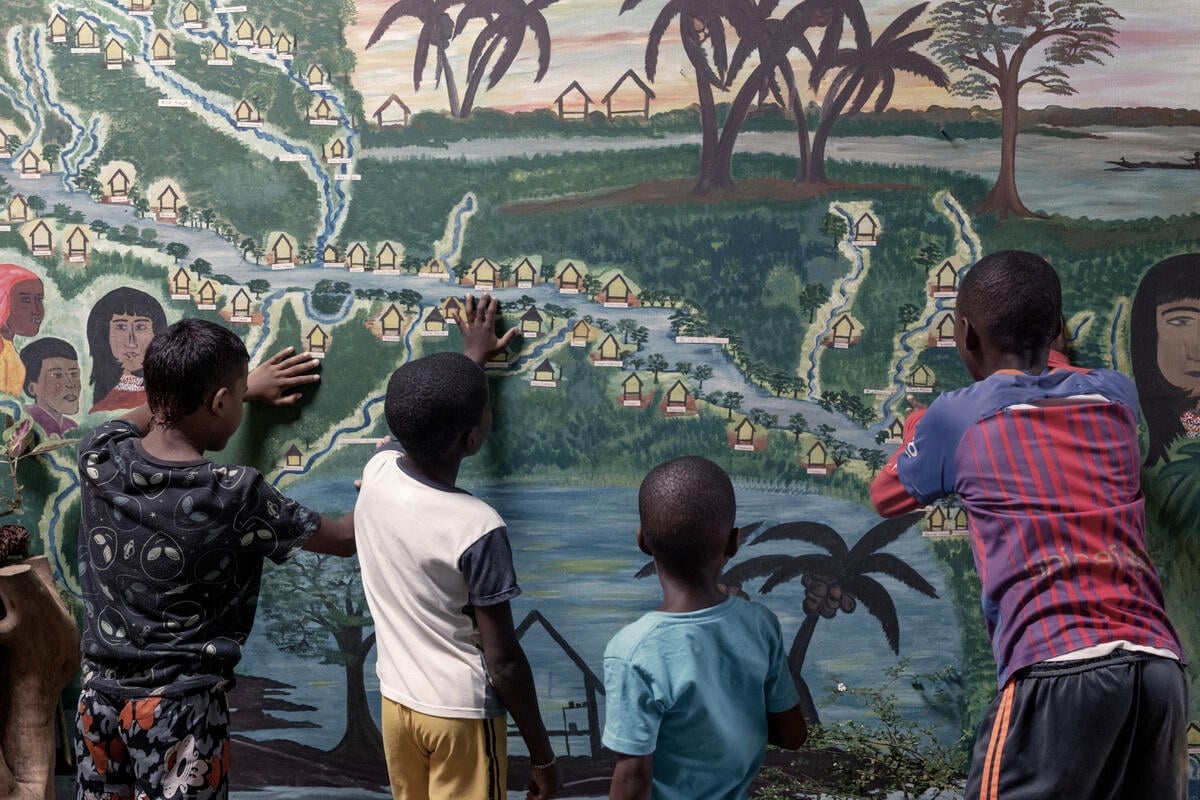 Children look at a mural depicting communities living along a river.