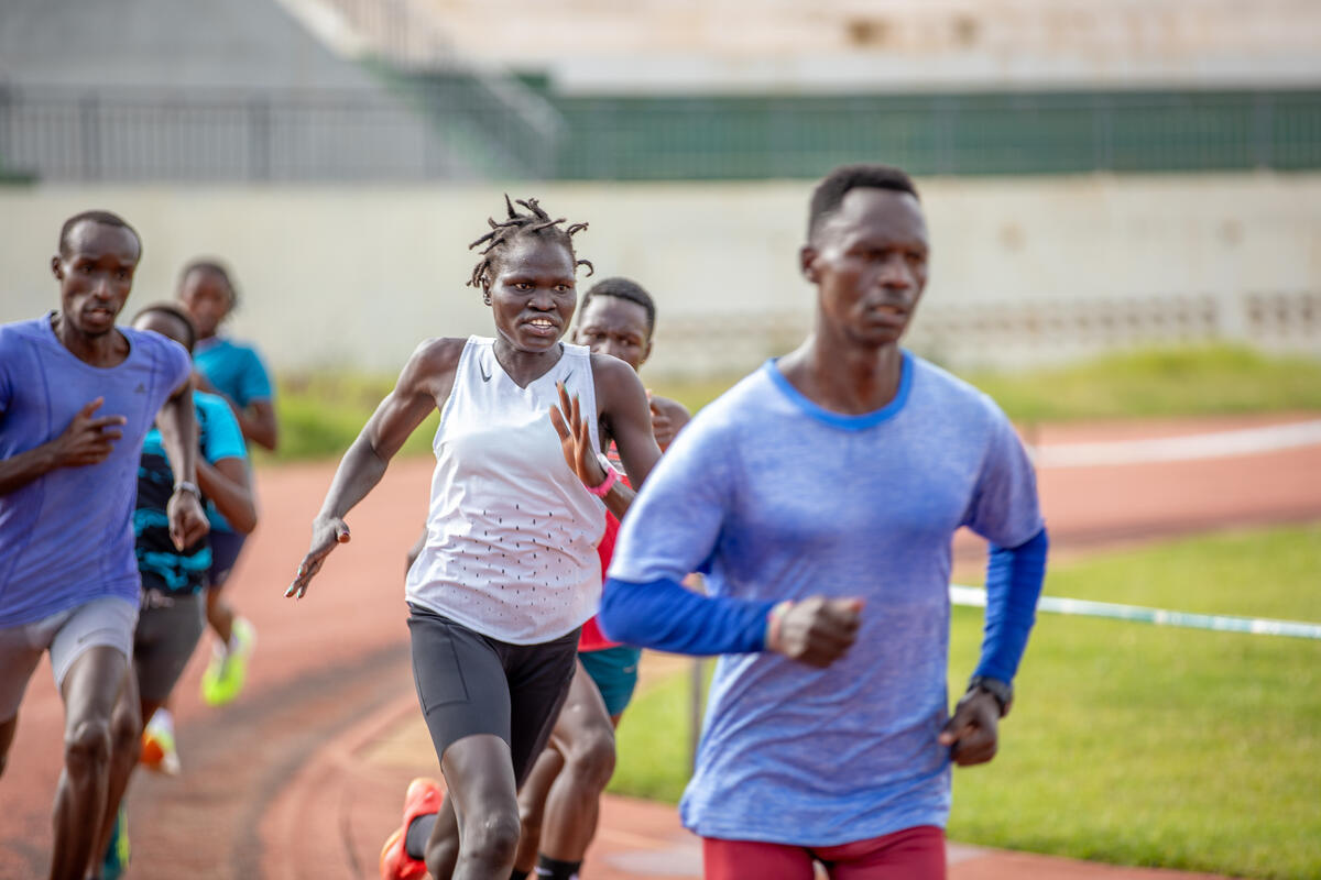 A young woman races around a running track in second place amongst other runners.