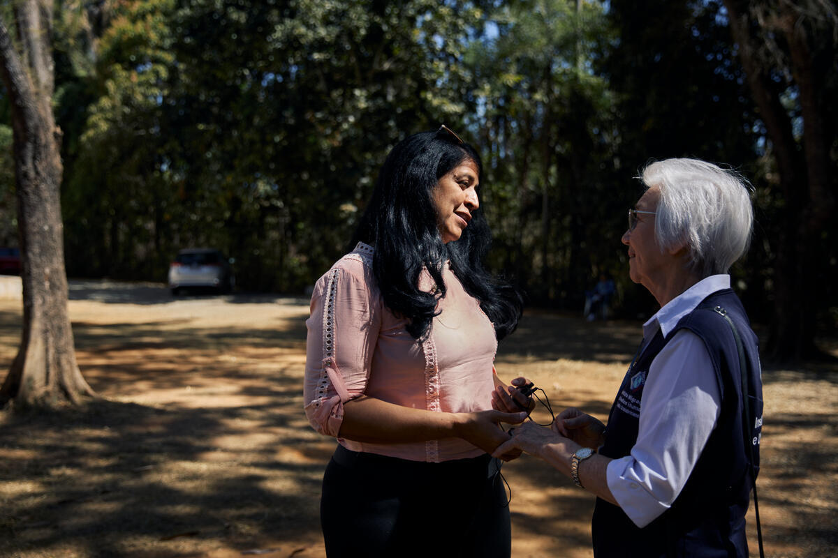 Two women hold hands as they talk outside in a shady garden