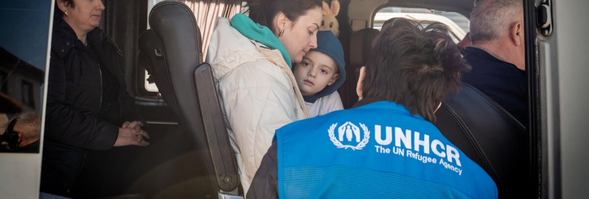 A UNHCR staff member speaks with a Ukrainian refugee mother and young boy on a bus.