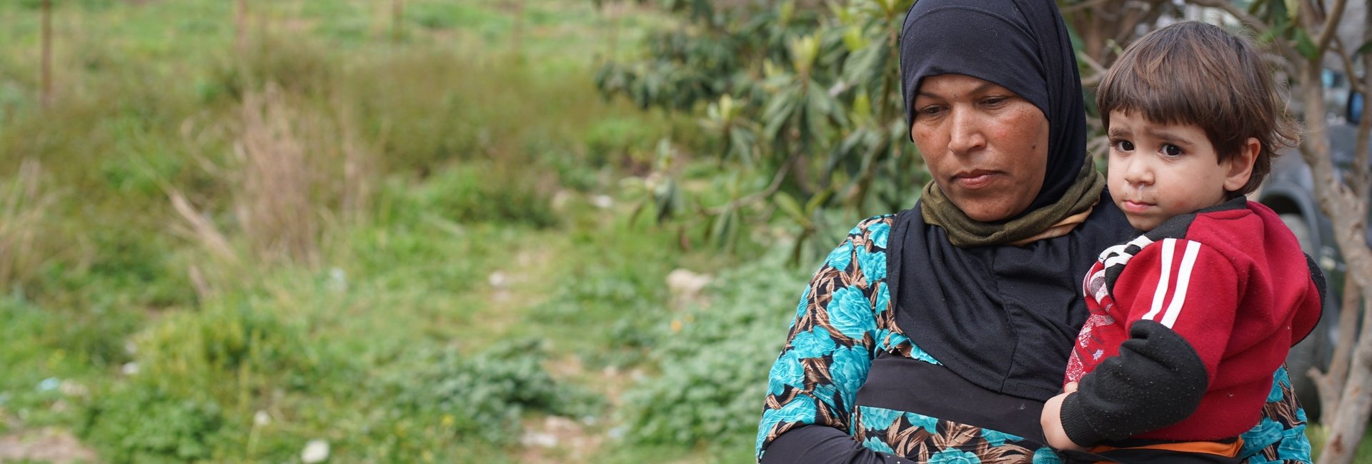 A Syrian woman holds her young nephew in a field near their home