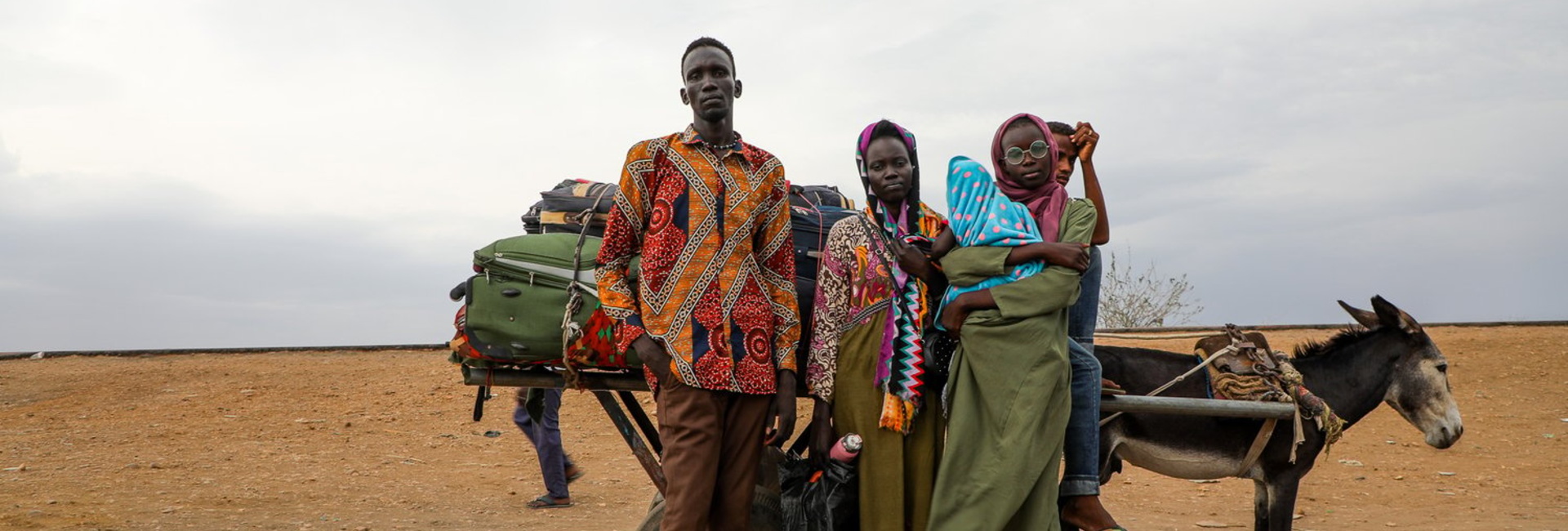 A South Sudanese returnee and his family stand with a donkey and cart carrying their belongings.