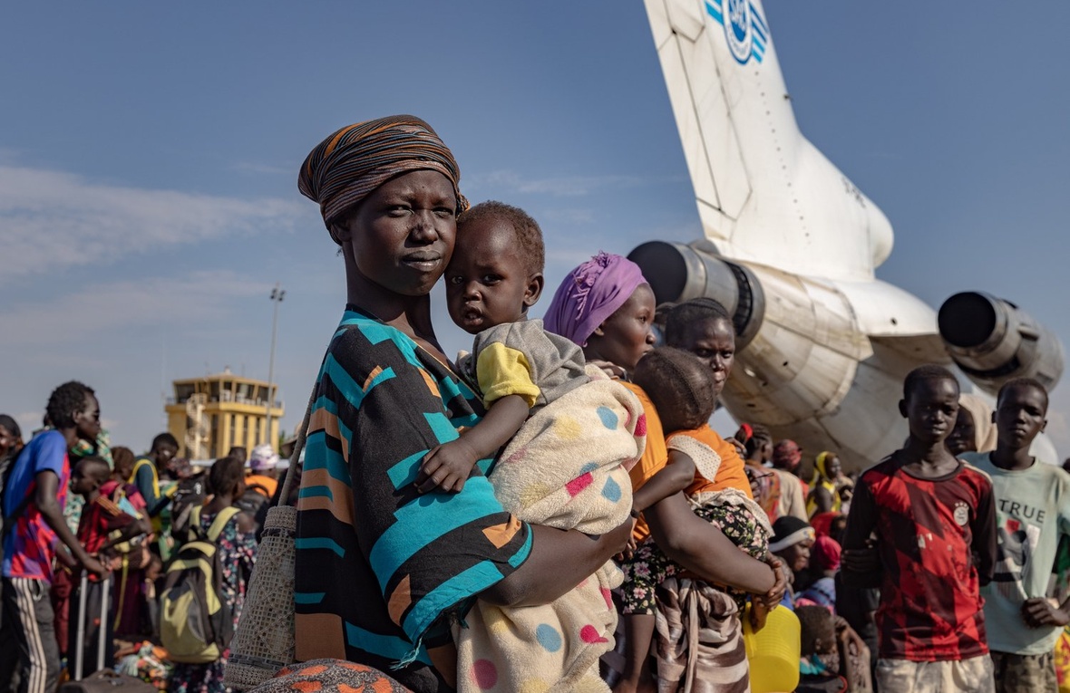 A woman holds her baby daughter surrounded by many other people near a plane.