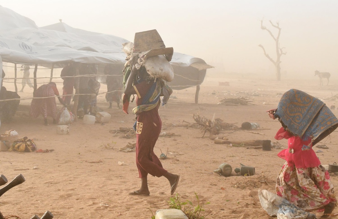 A woman and a child carry their belongings as they seek shelter during a sandstorm.