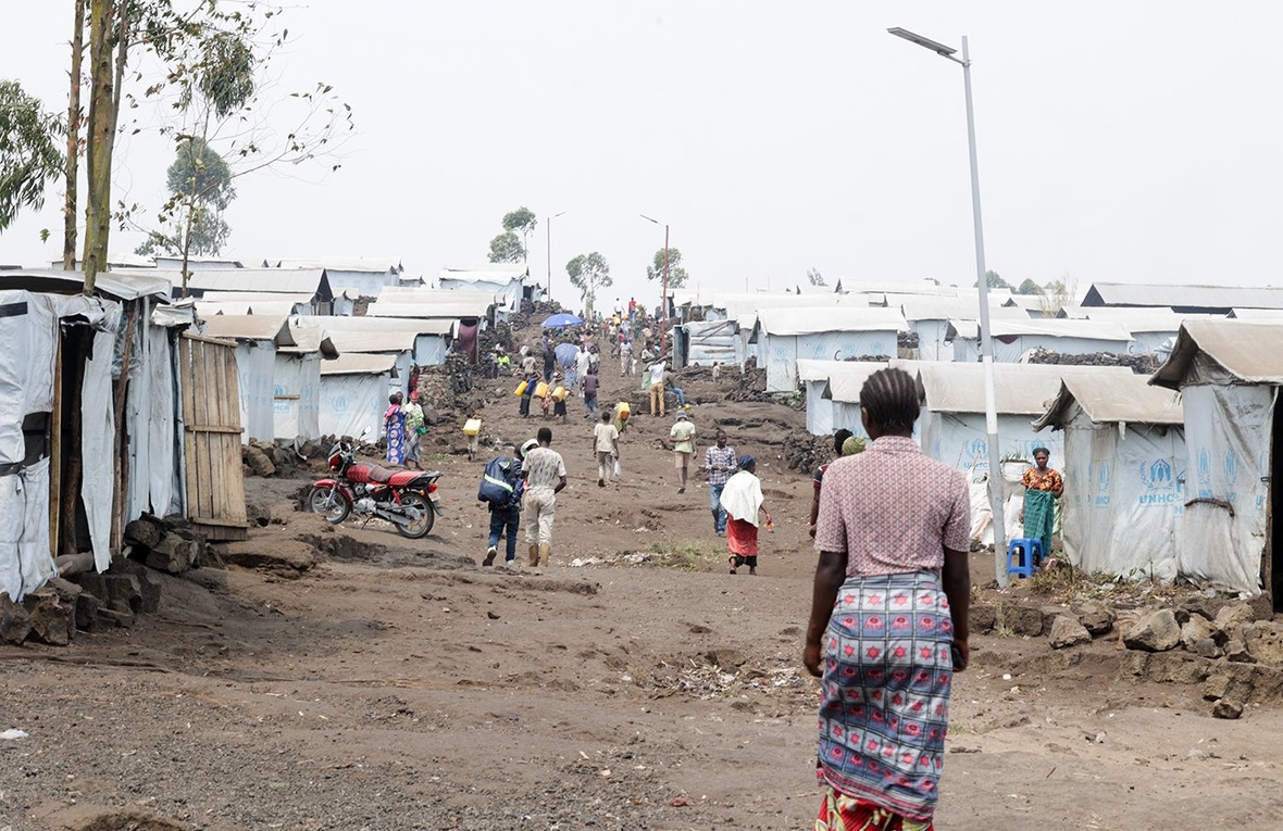 People in ones and twos walk over the undulating dry ground through a camp for internally displaced people 