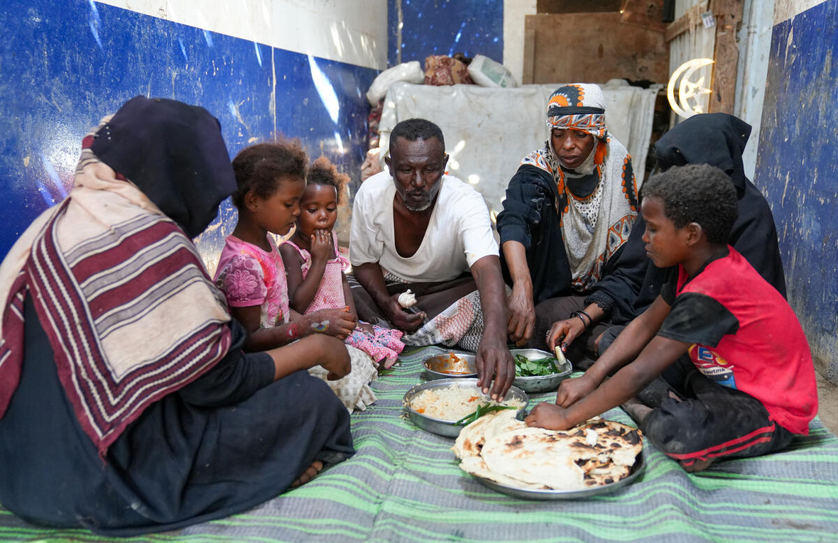 A family share a meal, seated on the floor