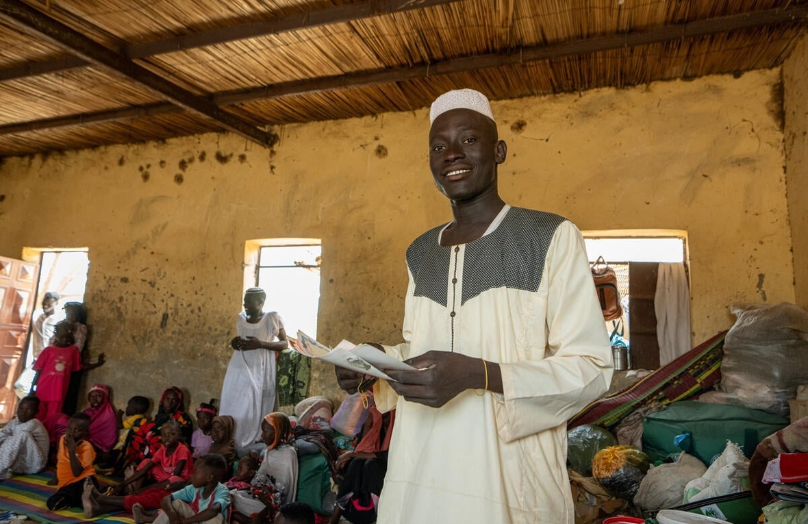 A young man holds some documents in a crowded room.