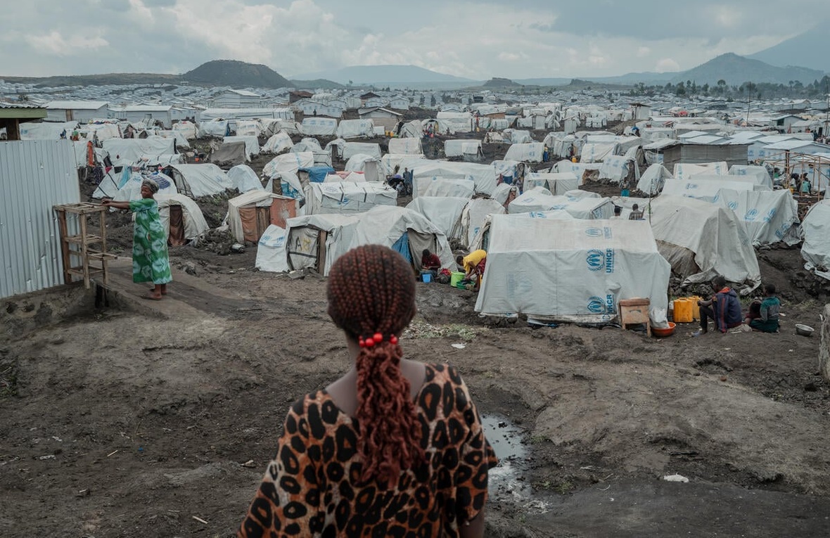 A rear view of a woman standing on muddy ground in front of hundreds of tents stretching to the horizon.