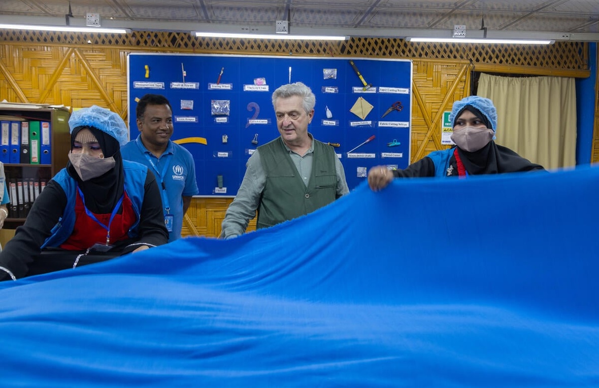 Four people stand holding a large blue piece of fabric in a production centre