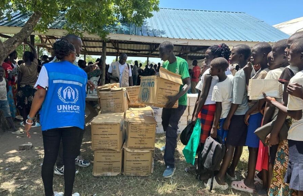 Women and children line up to receive aid packages in boxes from a UNHCR staff member.