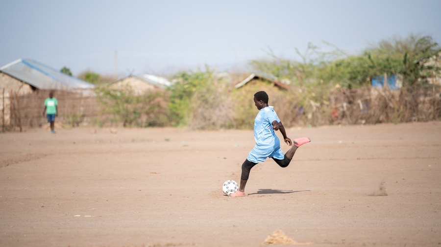 A girl prepares to kick a football on a dusty pitch.