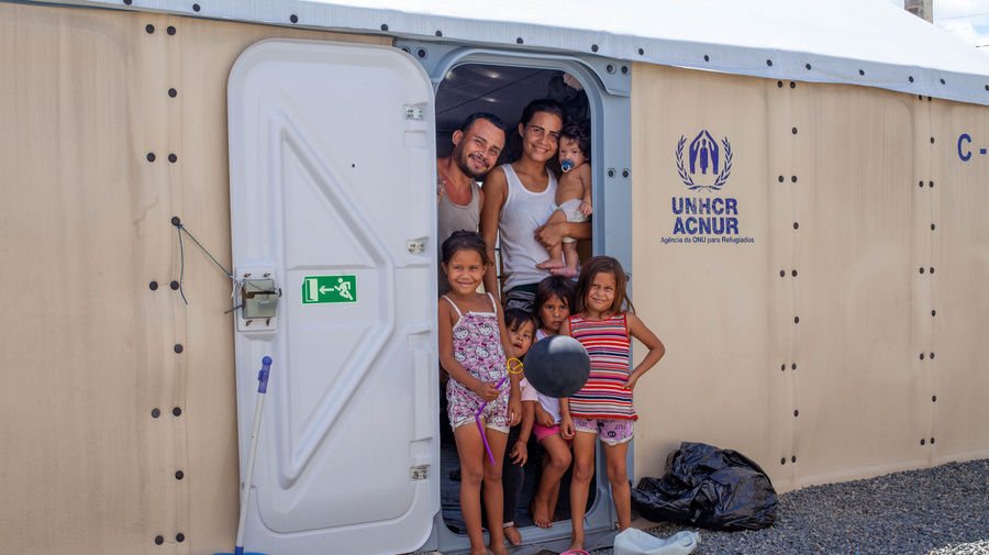 A Venezuelan refugee family stands together in front of the door of a UNHCR shelter in Brazil.