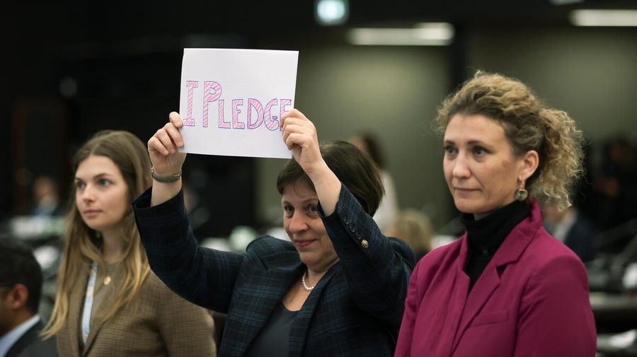 Three individuals stand together, one holds up a sign that reads 'I pledge'.
